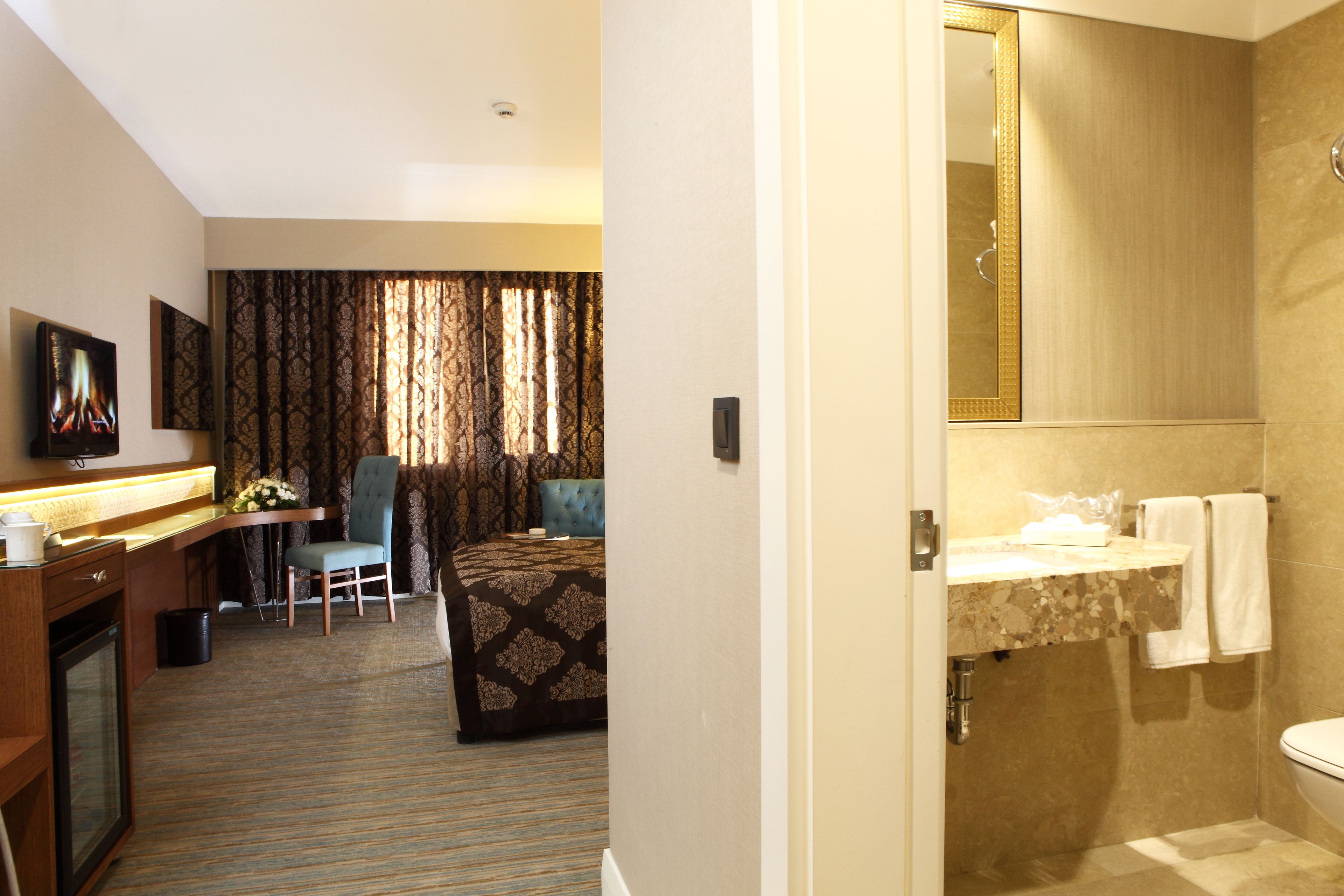 A hotel room with a bed, a desk with a chair, a television, and a bathroom with a sink and toilet.