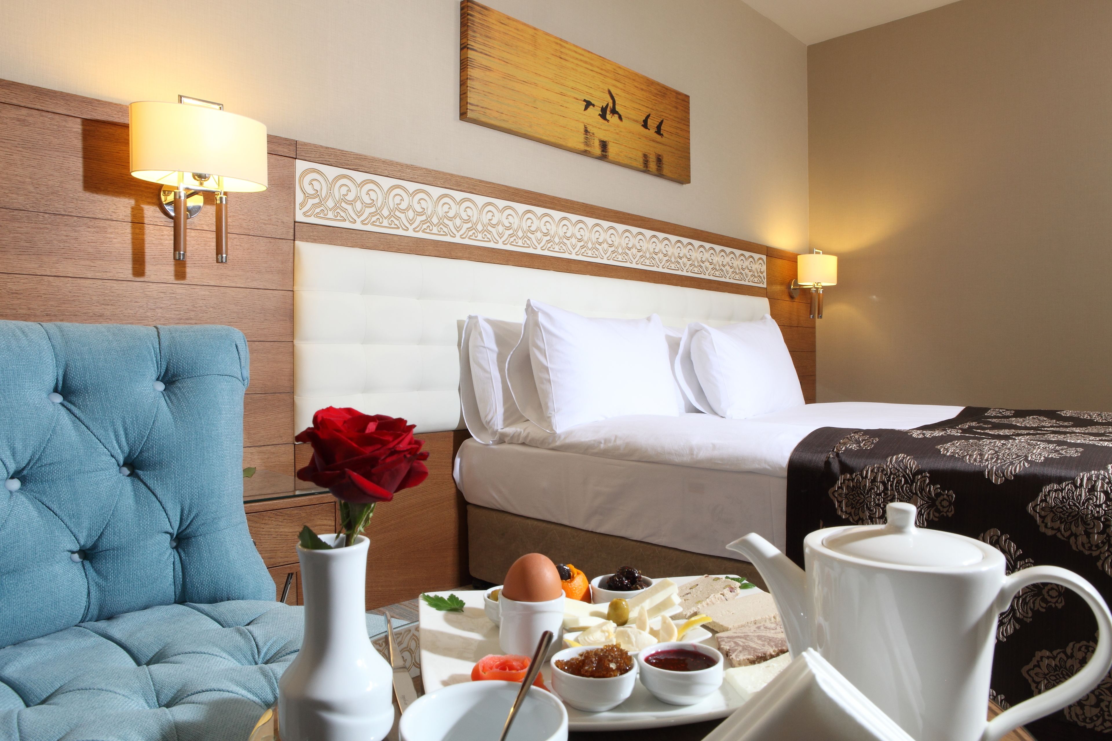 Habitación de hotel con cama, un sillón azul, una mesa de comedor con alimentos para el desayuno y un cuadro en la pared.