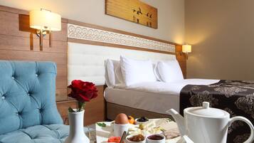 Habitación de hotel con cama, un sillón azul, una mesa de comedor con alimentos para el desayuno y un cuadro en la pared.