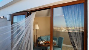 Una habitación de hotel con balcón, una mesa de comedor con sillas, un sofá y vistas a la ciudad.