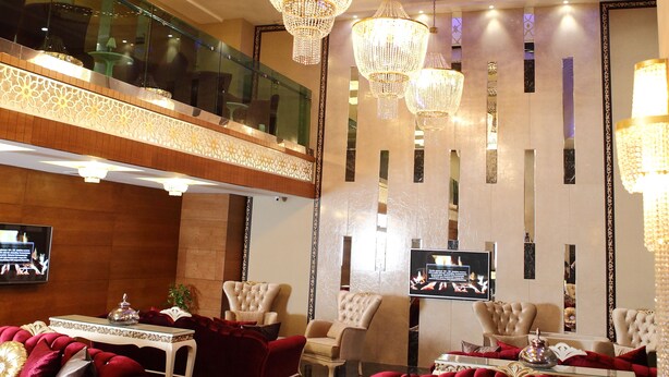 Un lobby de hotel lujoso con candelabros ornamentales, sofás rojos cómodos y un techo alto con diseños intrincados.