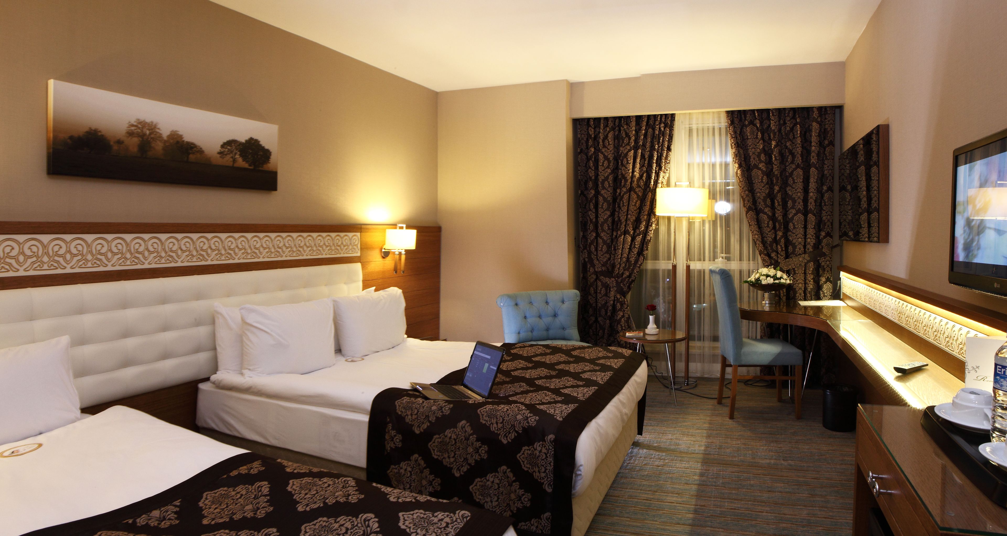 A hotel room with two beds, a desk, a chair, a TV, and a window with curtains.