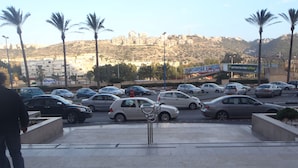 A parking lot with multiple cars and a pedestrian walking. - Almog Studio (Haifa)