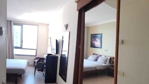 A hotel room with a bed, a desk, a chair, a television, and a window. - Almog Studio (Haifa)