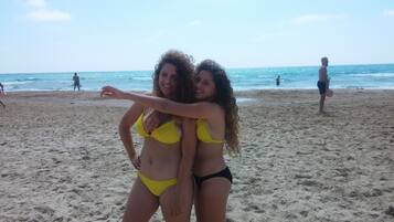 Ein Strand mit Personen im Hintergrund und zwei Personen in gelb-schwarzen Bikinis, die sich im Vordergrund umarmen.