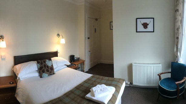 A hotel room with a bed, bedside tables, a chair, a radiator, and a window with curtains. - Loch Shiel Hotel (Acharacle)