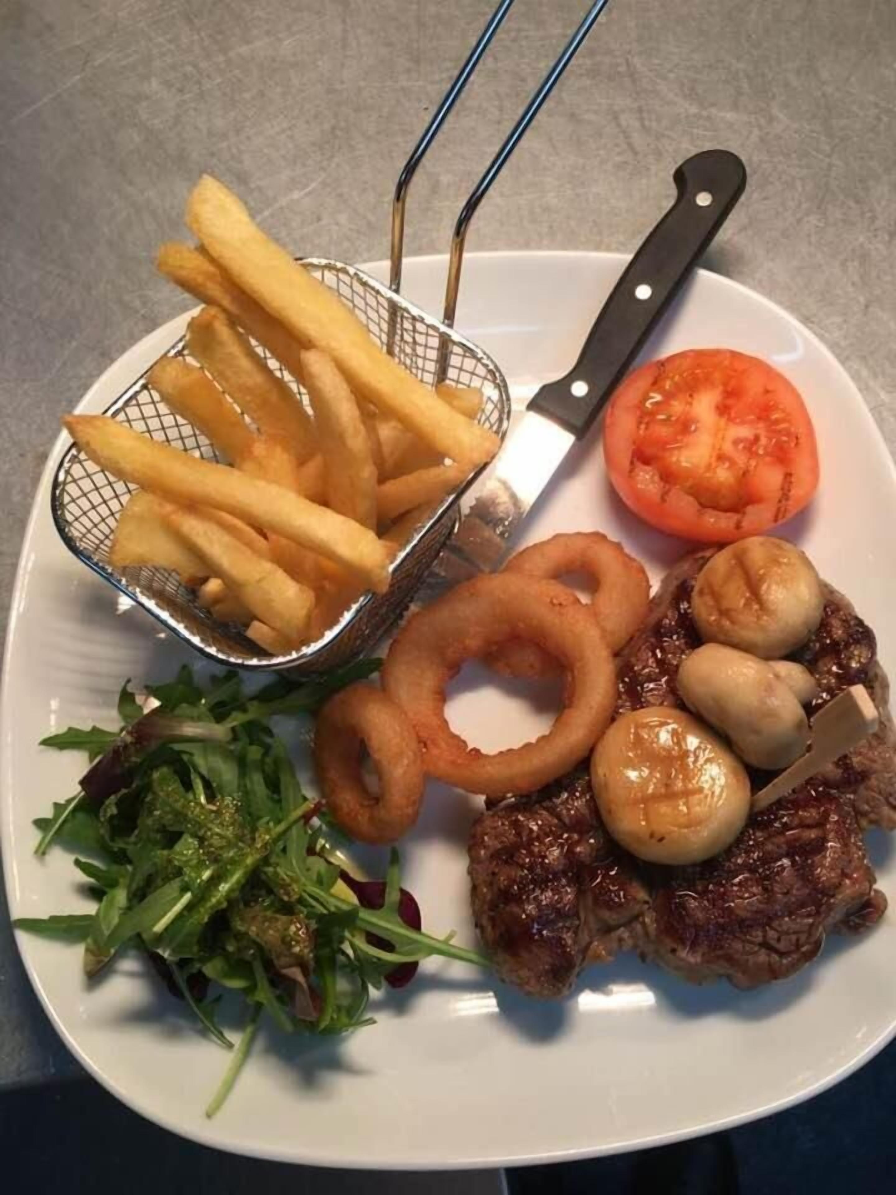 A plate with a steak, mushrooms, onion rings, a tomato, and fries.