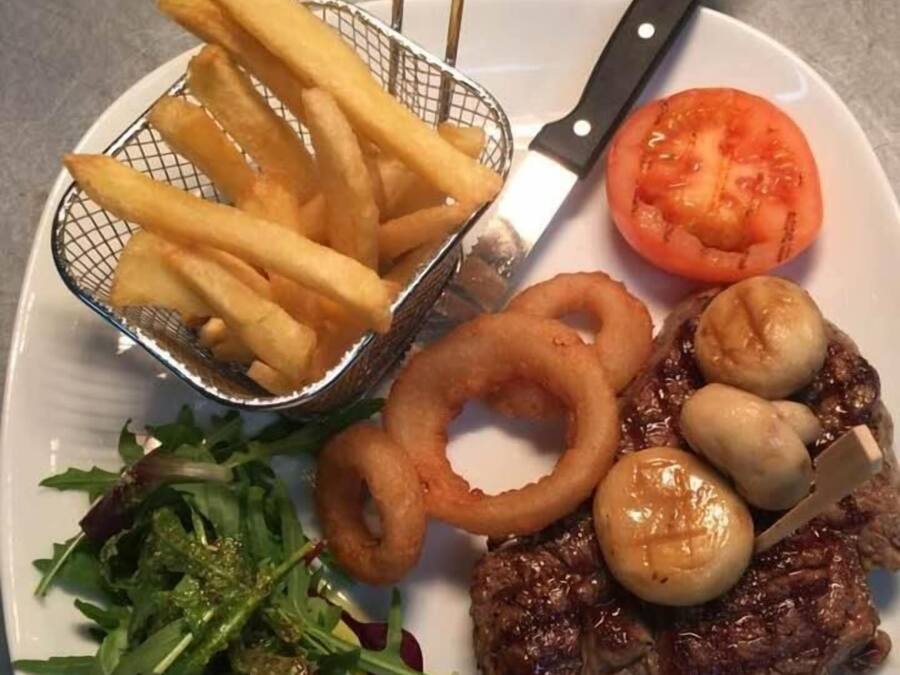 A plate with a steak, mushrooms, onion rings, a tomato, and fries.