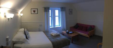 A bedroom with a bed, a bedside table, a window with curtains, a red sofa, and wall-mounted lights.