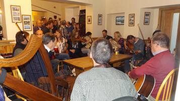 A group of people playing string instruments in a room with wooden furniture and framed pictures on the walls.