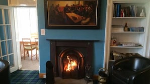 A room with a fireplace, a painting above it, a bookshelf, and a plaid carpet. - Loch Shiel Hotel (Acharacle)