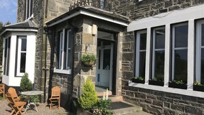 A stone building with a traditional entrance, a small porch with wooden chairs, and potted plants. - Loch Shiel Hotel (Acharacle)