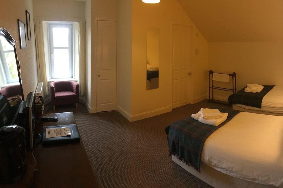 A hotel room with two beds, a desk with a chair, a wardrobe, and a window.