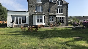 A stone house with a large lawn and outdoor seating area. - Loch Shiel Hotel (Acharacle)