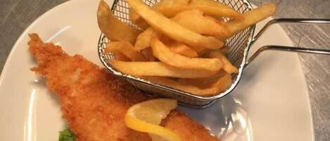 Un plato con un filete de pescado empanizado, papas fritas y guisantes verdes.
