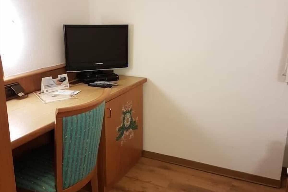 Une petite pièce comprenant un bureau en bois, une chaise, un téléviseur et un meuble de rangement.