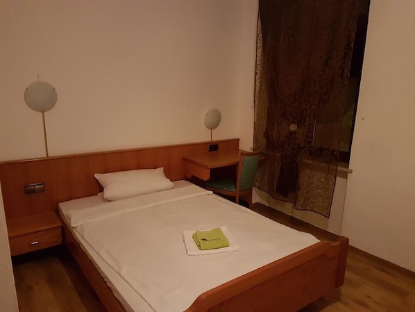 Una habitación de hotel con una cama de madera, una mesita de noche y una ventana con cortina.