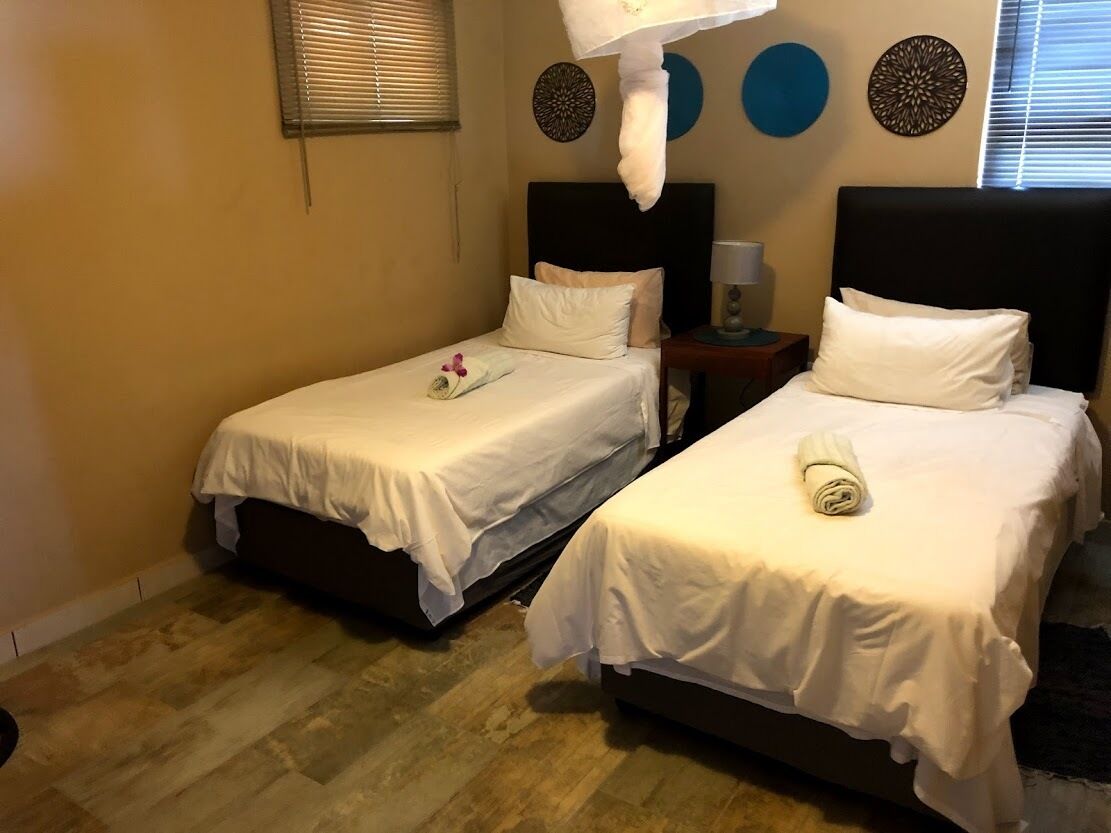 A hotel room with two single beds, a nightstand, a lamp, and decorative wall art.