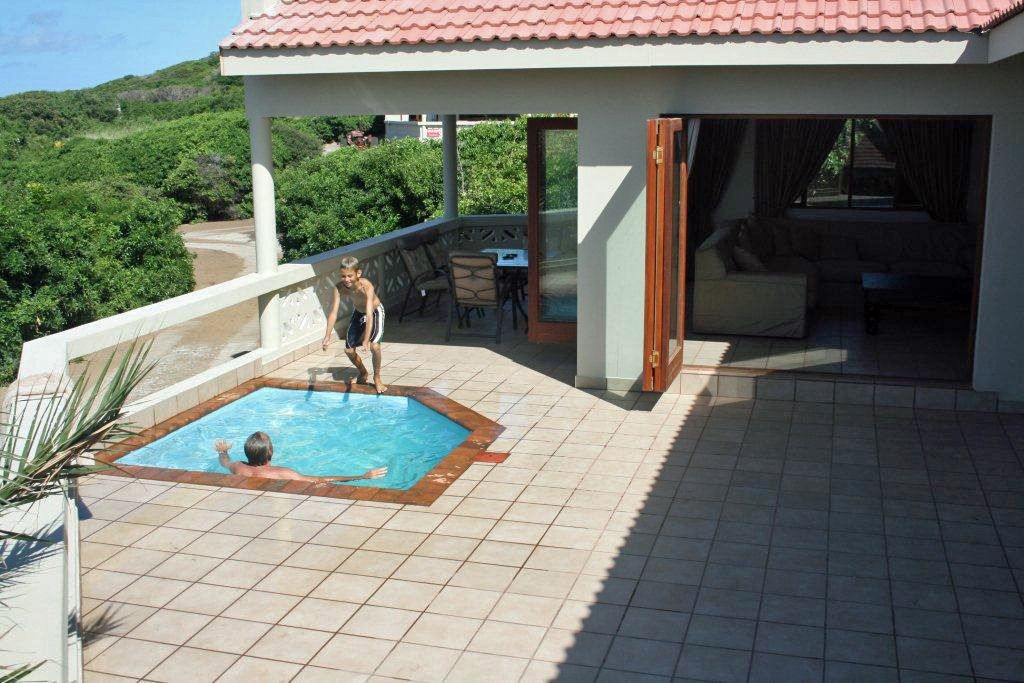 A pool area with a child playing, a covered seating area, and a view of the surrounding greenery.