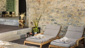 A stone wall with two wooden lounge chairs and a small table with a plant. - Ariá Estate Suites & Spa (East Mani)
