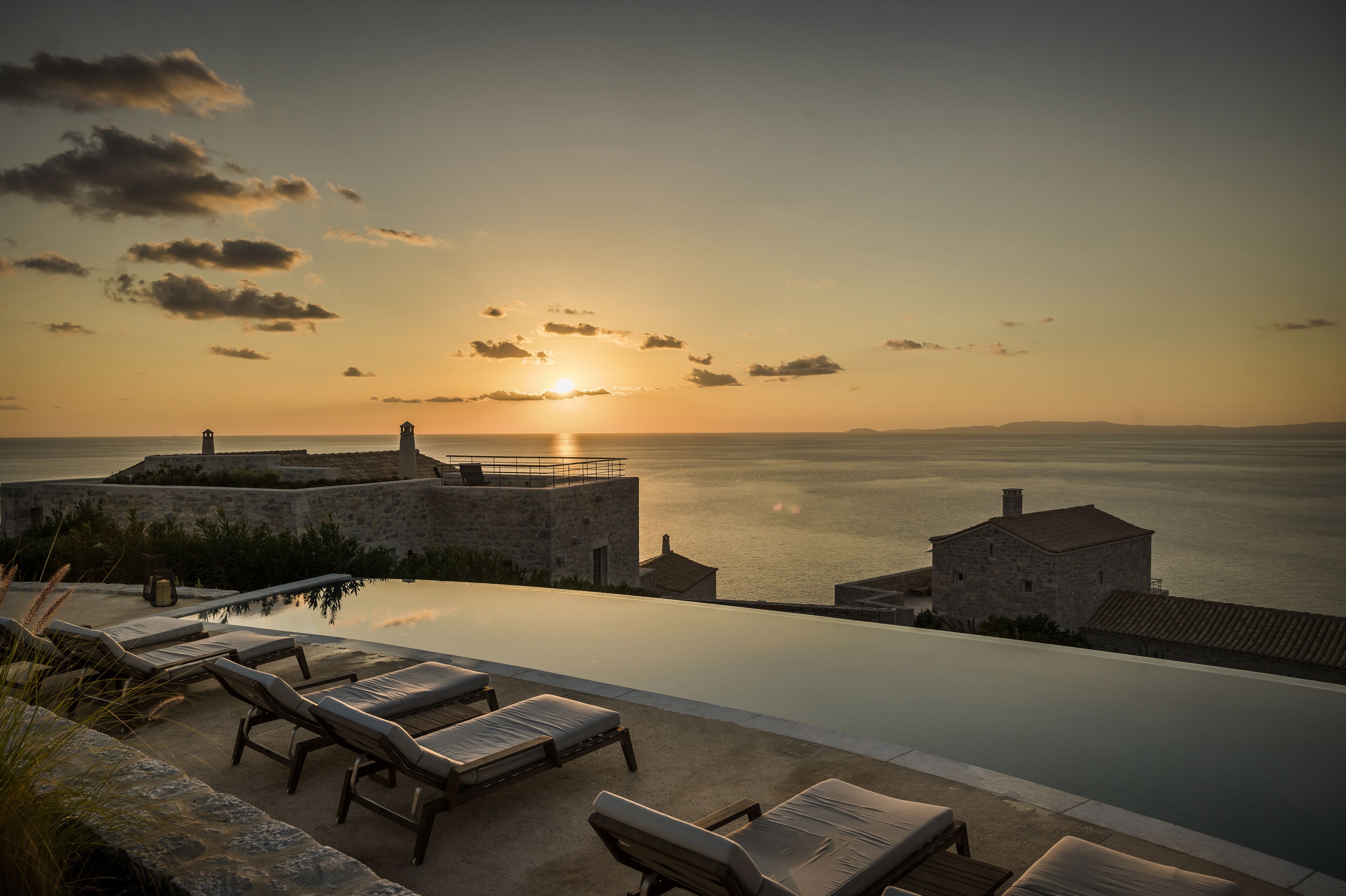 An infinity pool with lounge chairs overlooking the sea at sunset.