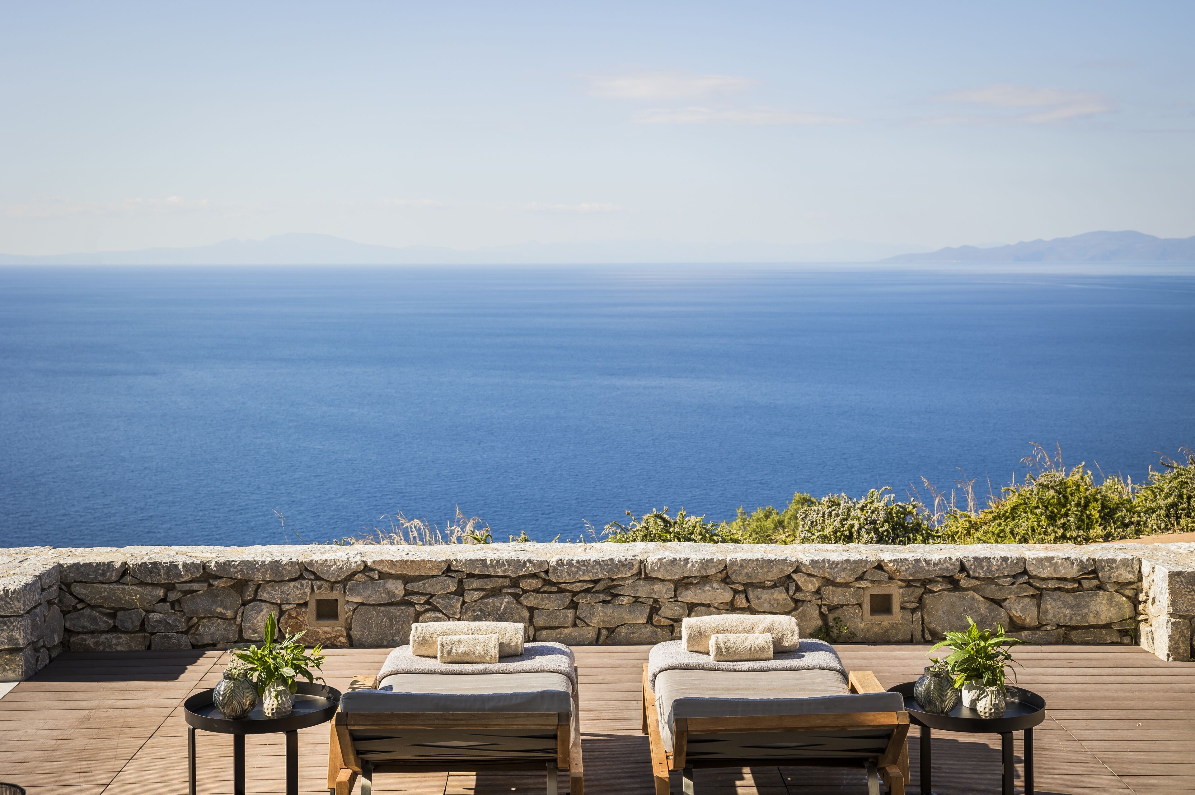 A deck with two lounge chairs and a table, overlooking a body of water and distant mountains.