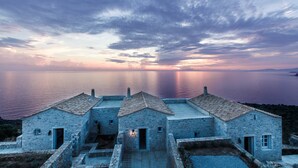 A stone building with a tiled roof overlooking a calm sea at sunset. - Ariá Estate Suites & Spa (East Mani)