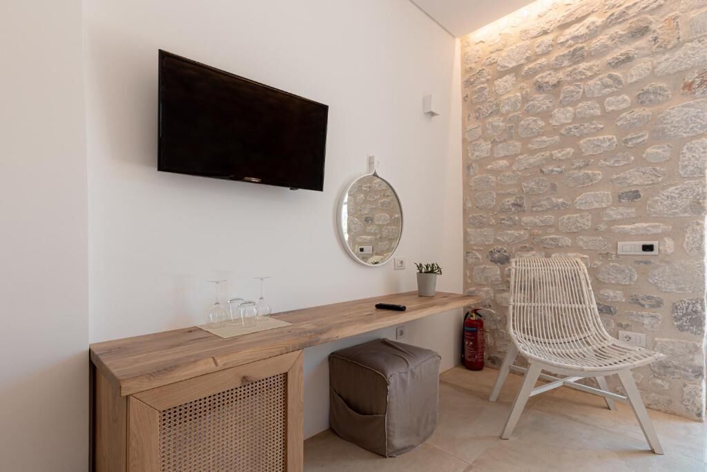 A modern room with a wooden console table, a mounted TV, a stone wall, a white woven chair, and a small potted plant.