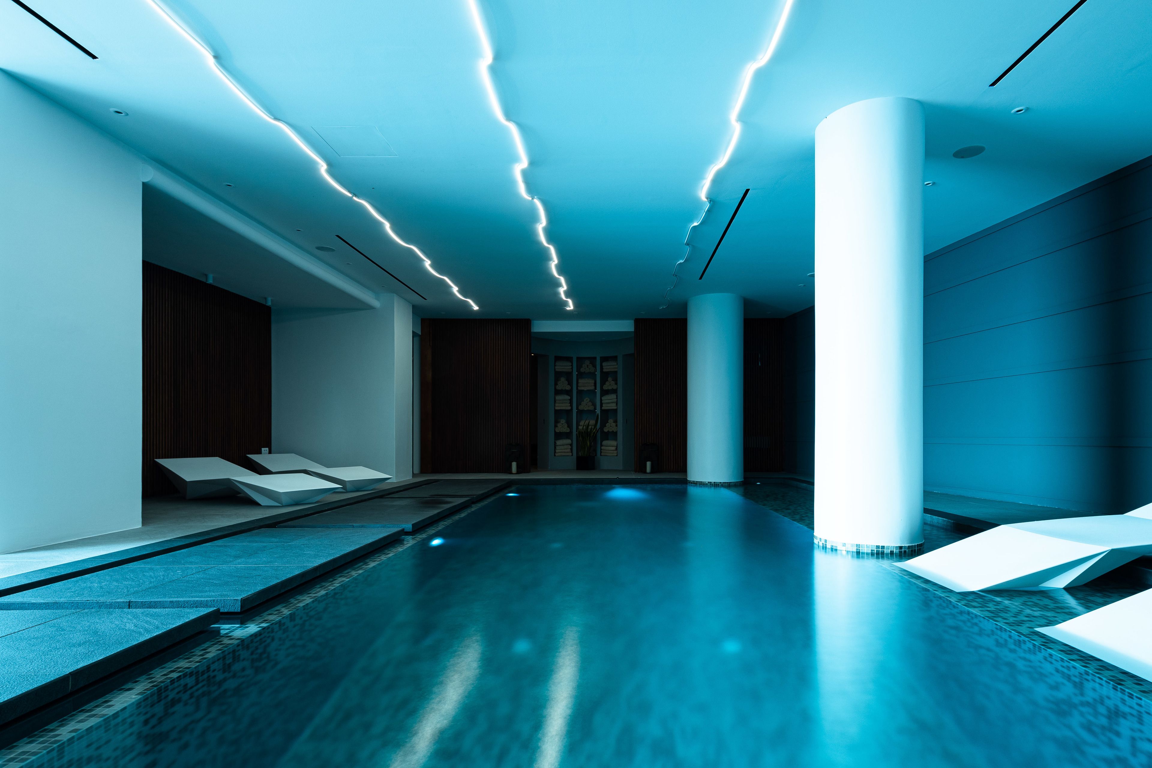 Une piscine intérieure moderne au design minimaliste, avec un grand bassin rectangulaire, des colonnes blanches et un mur en bois en arrière-plan.