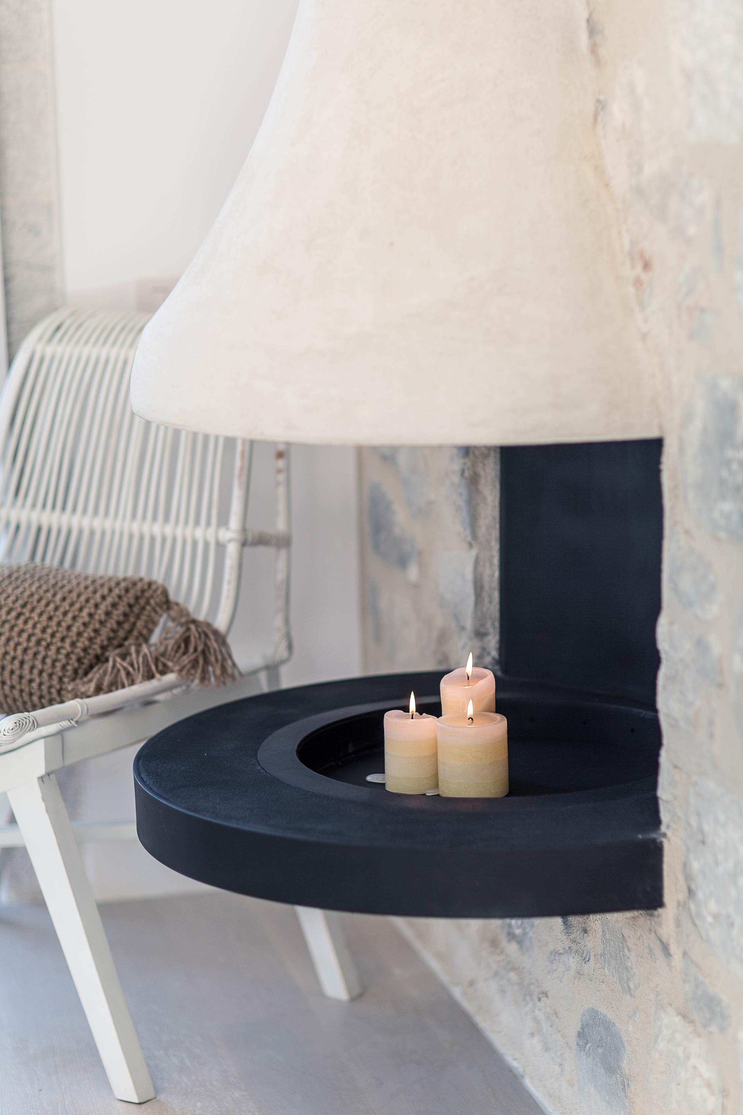 Un interior moderno con chimenea de piedra, una silla blanca y un estante negro con velas.