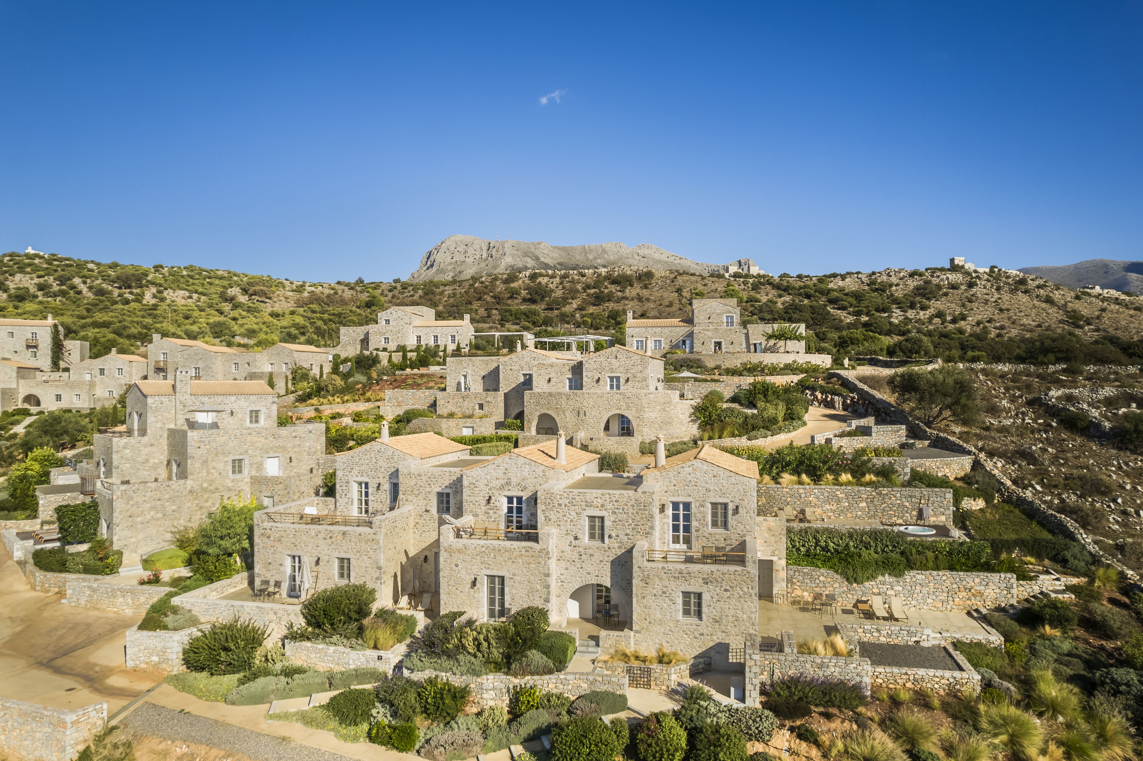 A stone-built village with terraced houses, a prominent hill in the background, and a clear blue sky.