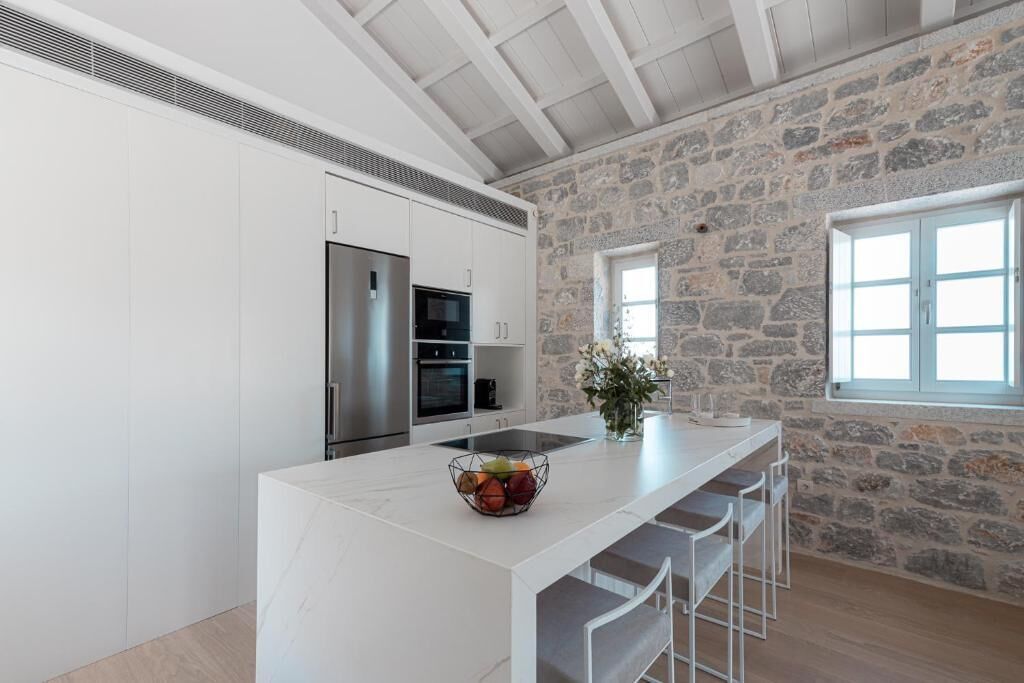 Una cucina moderna con mobili bianchi, una grande isola con sgabelli da bar, una parete in pietra e una finestra.