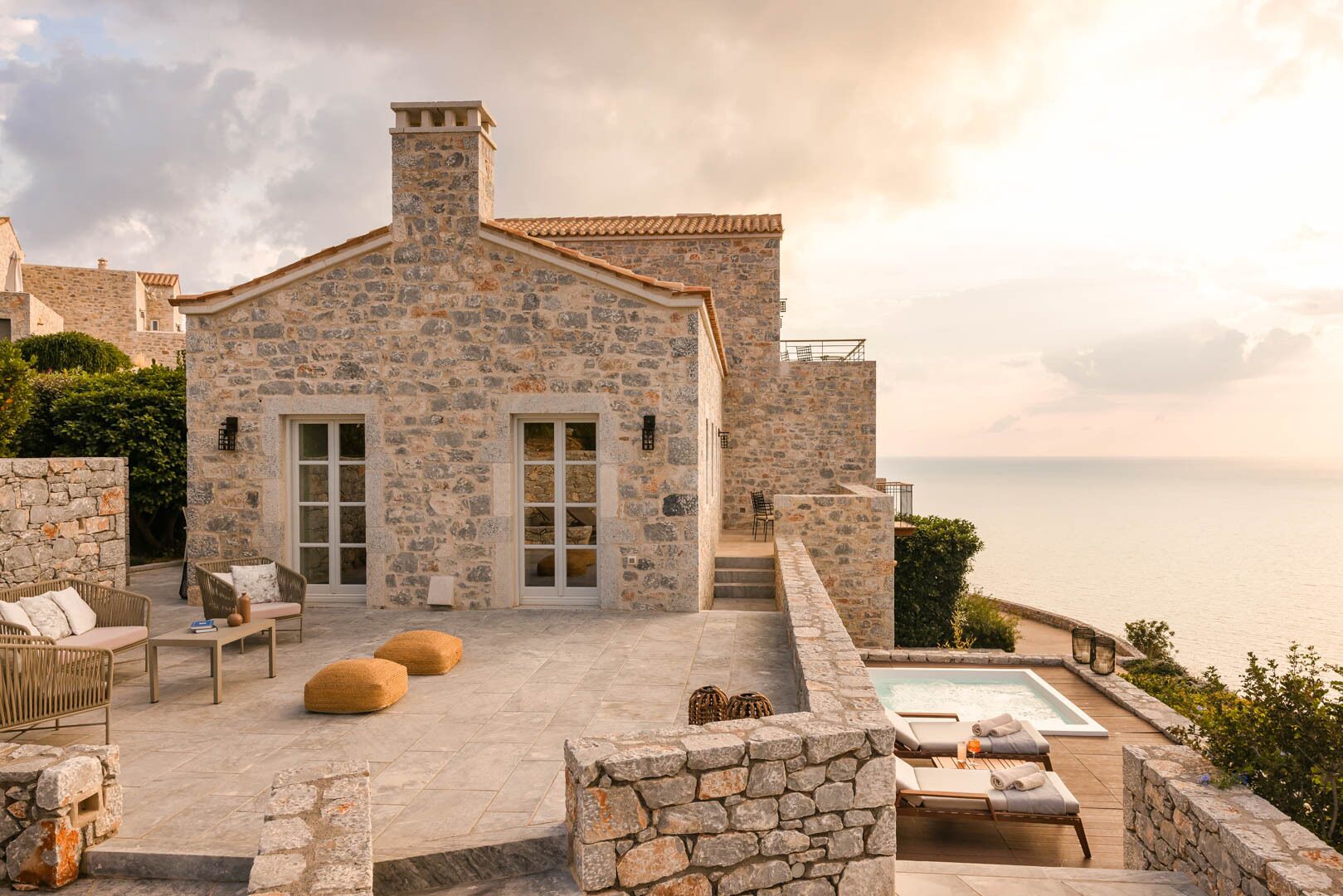A stone house with a pool, outdoor seating, and a view of the sea.