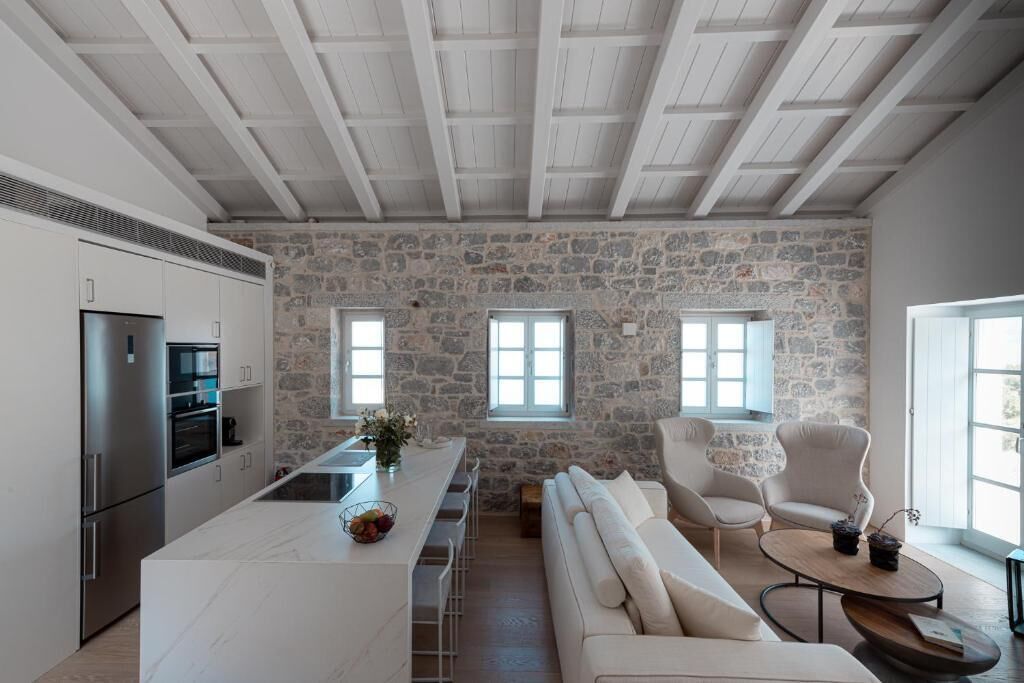 A modern kitchen with a stone wall, a white countertop, and built-in appliances. There is a bar area with stools and a sofa.