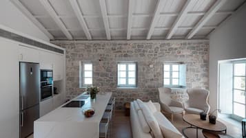 Una cocina moderna con pared de piedra, encimera blanca y electrodomésticos integrados. Cuenta con una barra con taburetes y un sofá.