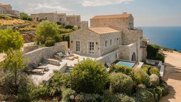 A stone villa with a pool, outdoor seating, and views of the sea.