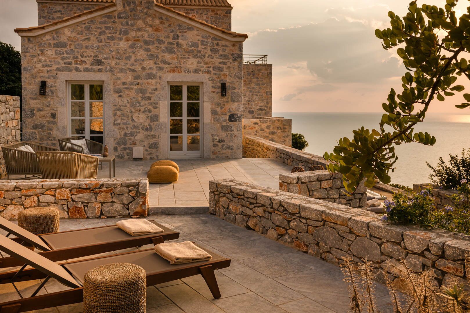 A stone building with a terrace, outdoor seating, and a view of the sea.