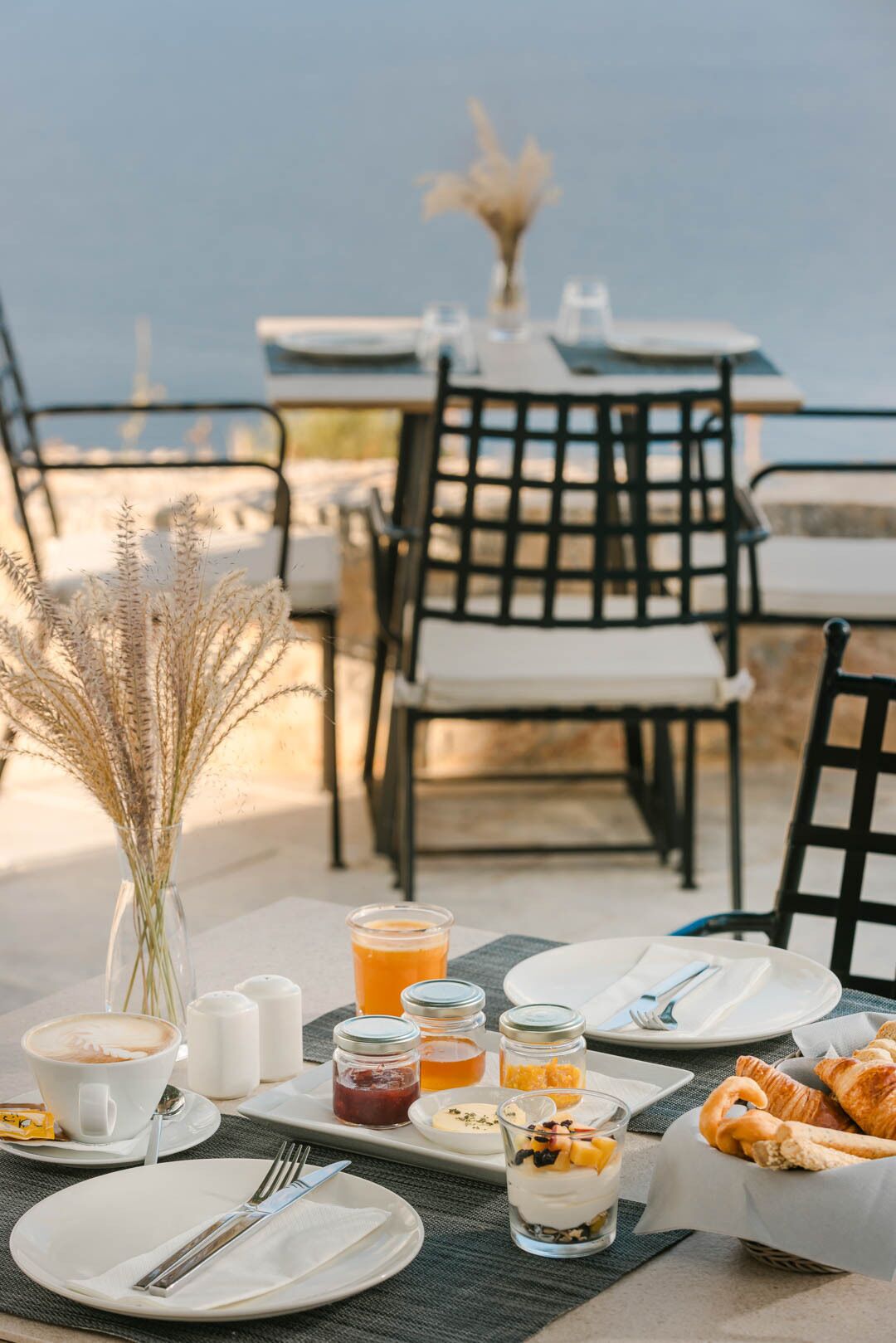 Mesa al aire libre lista para el desayuno, con croissants, fruta y bebidas.