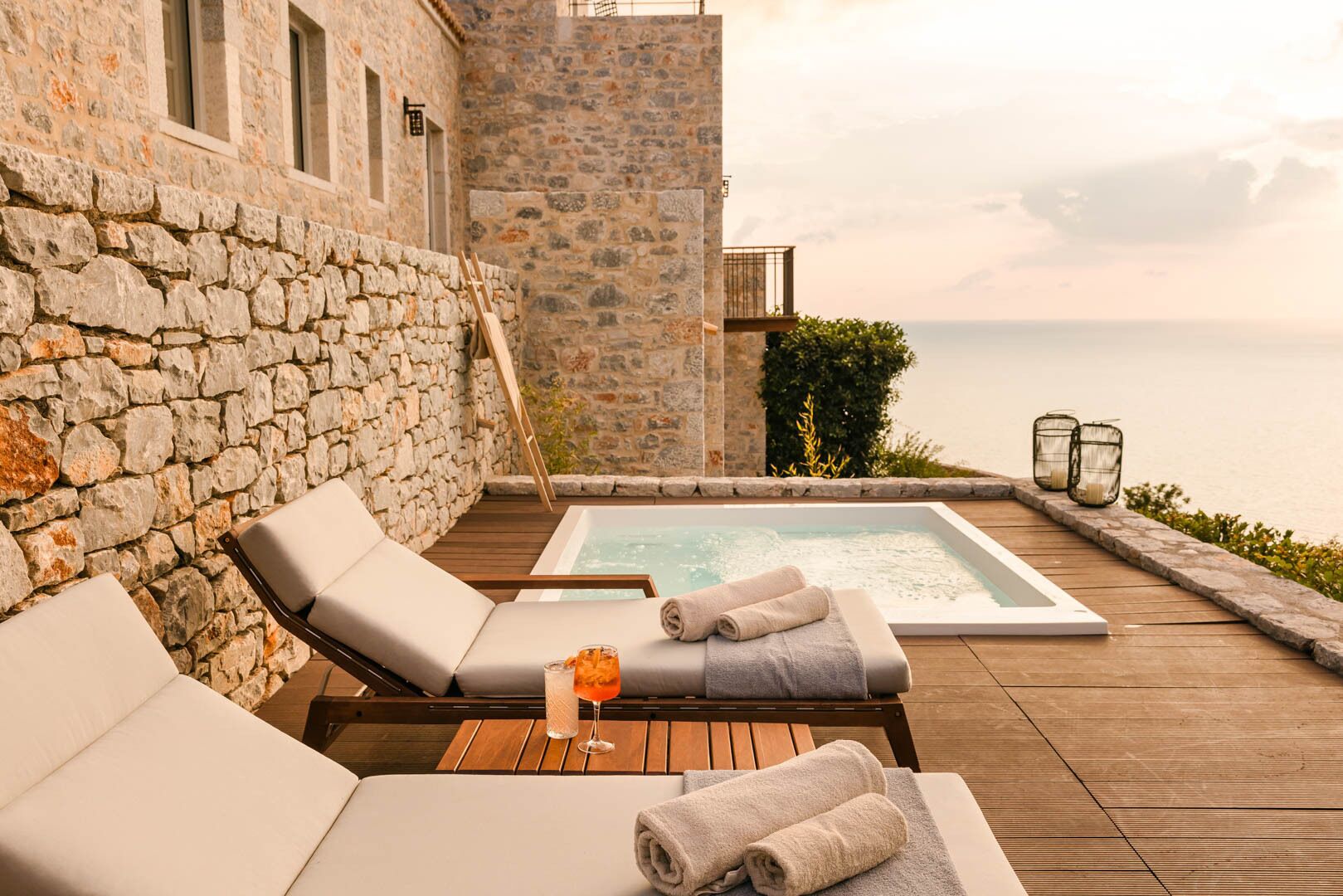 Un espacio al aire libre con paredes de piedra, un jacuzzi, sillones de descanso y vistas al mar.