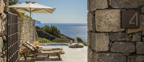 A stone-walled outdoor area with a pool, lounge chairs, and a view of the sea.