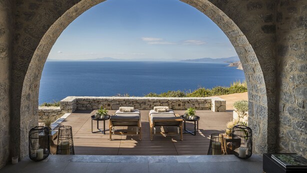 A stone archway overlooking a wooden deck with two lounge chairs and a table, set against a backdrop of the sea and distant mountains. - Ariá Estate Suites & Spa (East Mani)