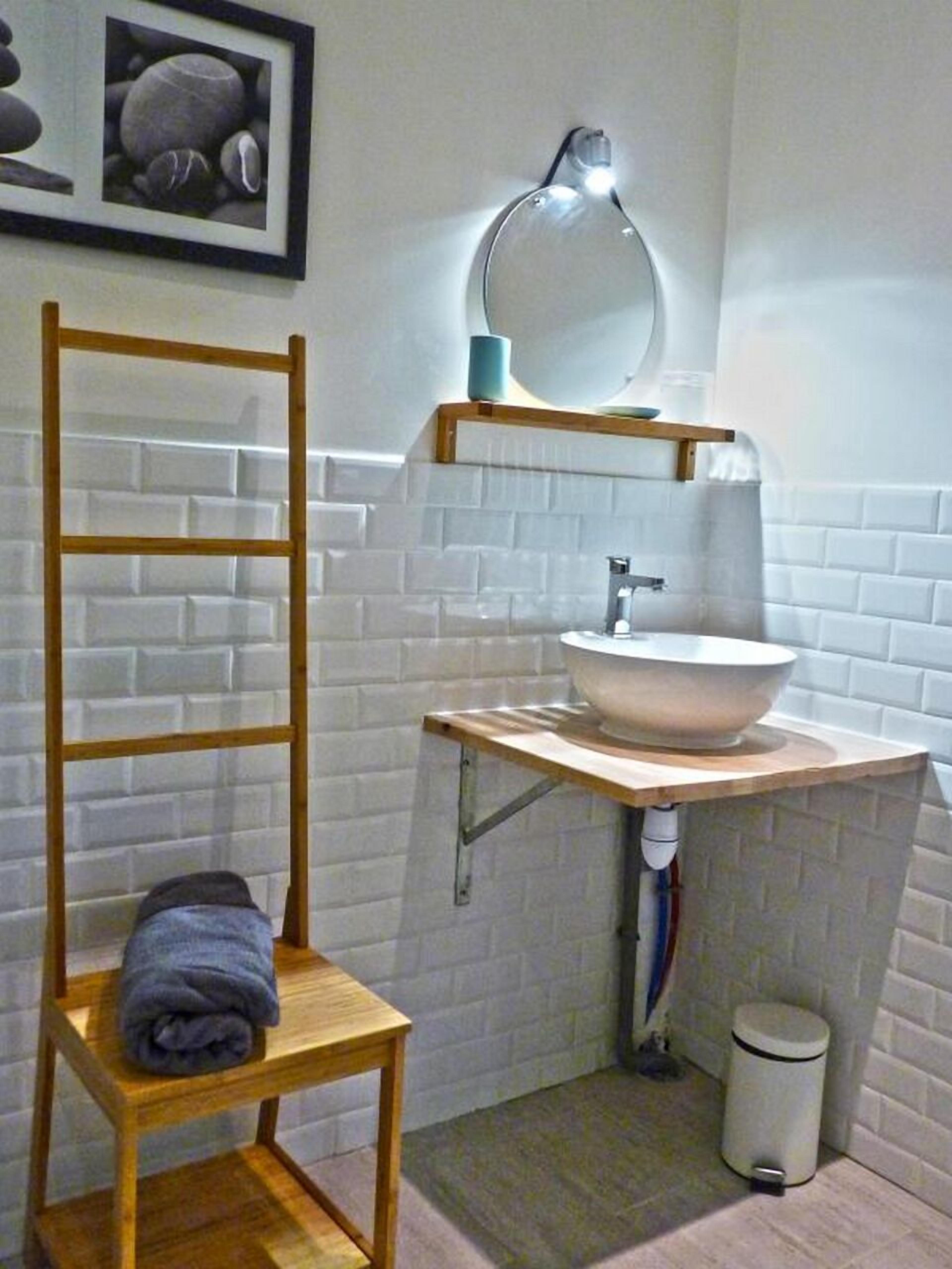 Un baño con una escalera de madera, un lavamanos con espejo y un cubo de basura.