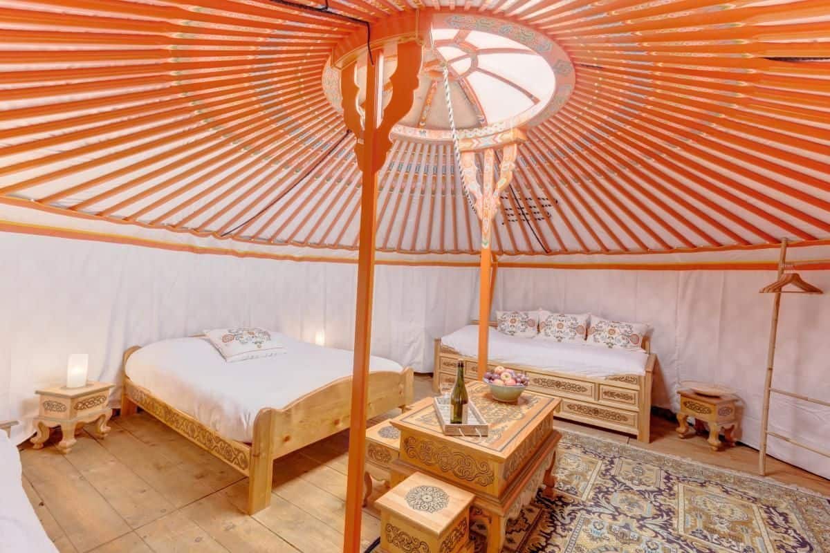 Una yurta tradicional con dos camas de madera, una mesa central y una alfombra estampada.