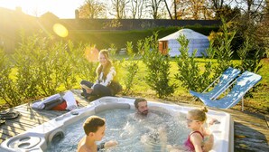 Un jacuzzi con cuatro personas, rodeado de follaje y una hamaca.