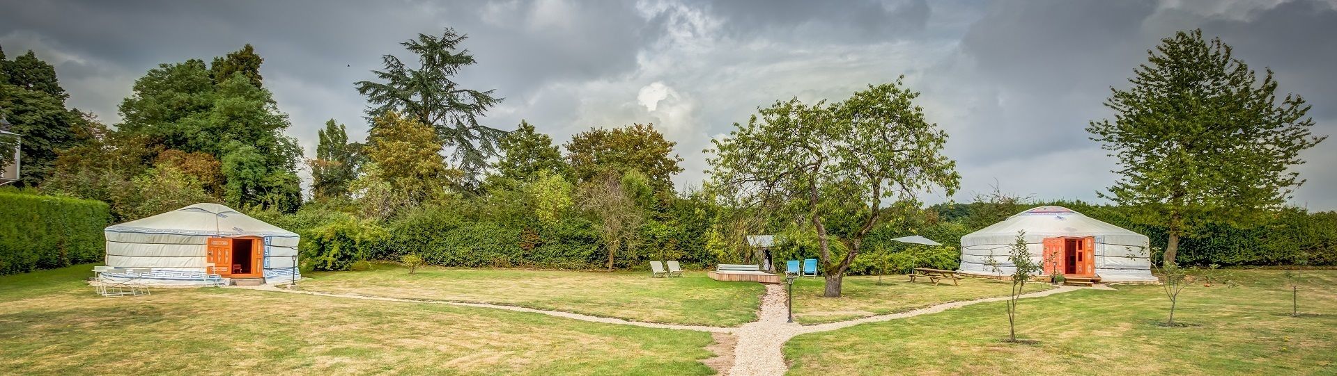 Duas yurts com portas abertas, um caminho pavimentado e vegetação ao redor.