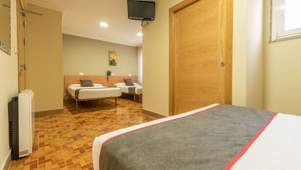 A hotel room with a large bed, two smaller beds, a wooden wardrobe, a television, and a telephone on the wall. - Casa Marín (Sanxenxo)
