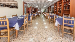 A dining area with tables set for a meal, wooden chairs, and shelves with bottles. - Casa Marín (Sanxenxo)