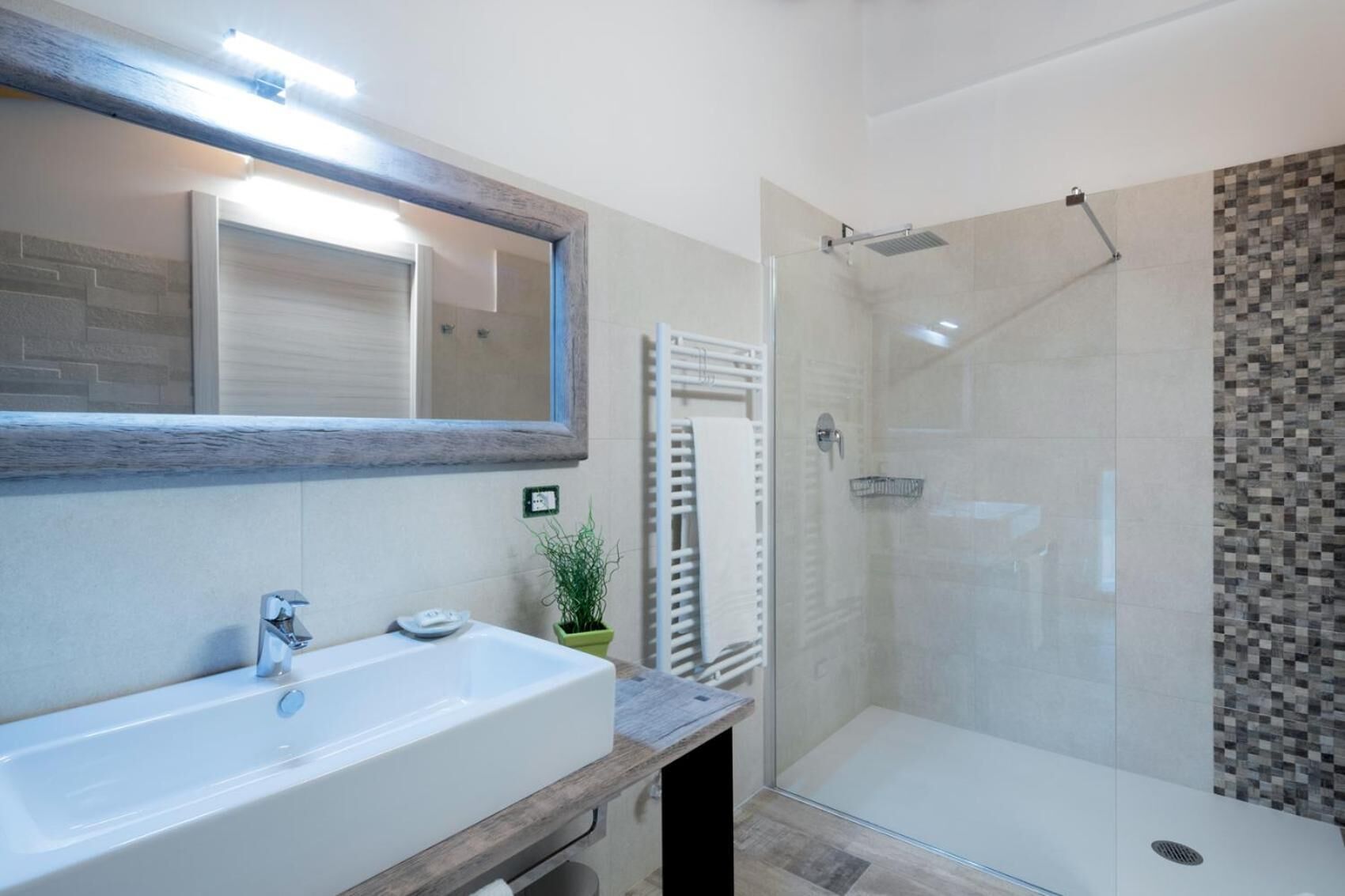 A modern bathroom with a large sink, a glass shower enclosure, and a tiled shower wall.