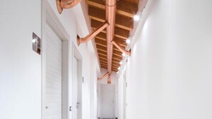 A hallway with white walls, wooden flooring, and exposed copper pipes on the ceiling. - Agriturismo Camisi (Cambiago)