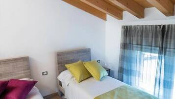 Een kamer met twee bedden, houten balken in het plafond en een raam met gordijnen.